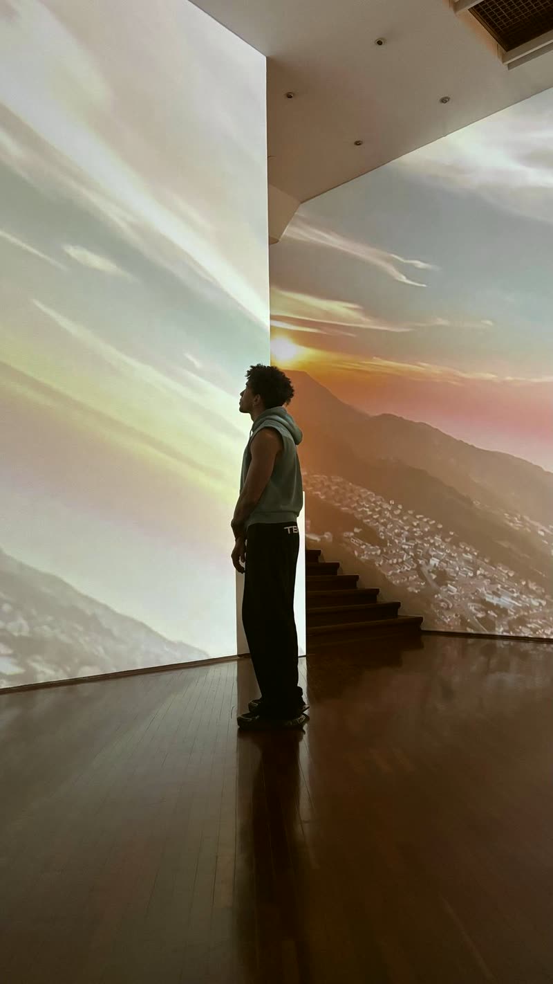 Geiser Elligon de pie frente a una proyección de montañas al atardecer en una galería